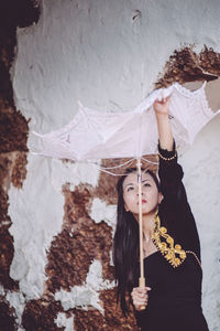 Woman adjusting umbrella while standing against brick wall