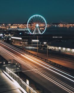 Light trails on illuminated city against clear sky at night