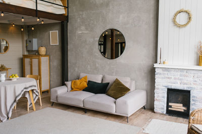 Gray sofa with pillows, a round mirror hangs on the wall in a modern scandinavian-style living room