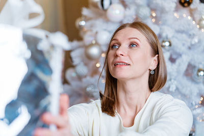 Portrait of smiling caucasian woman holding silver gift box near tree. a young