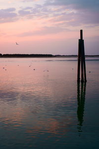 Wooden posts in sea against sky at sunset