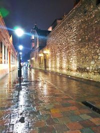 Wet street amidst illuminated buildings during rainy season