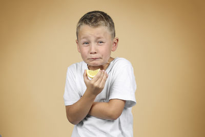 Portrait of boy eating lemon while making face against beige background