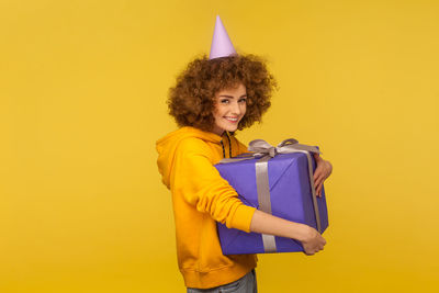 Young woman holding yellow while standing against orange background