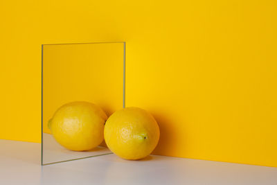 Yellow lemon is reflected in a mirror on a yellow background