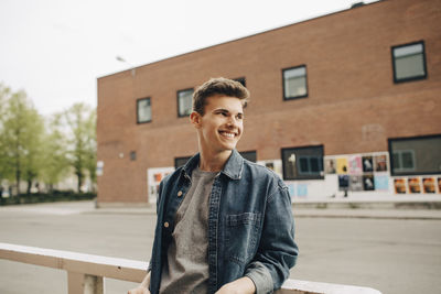 Smiling young man looking away while leaning on railing