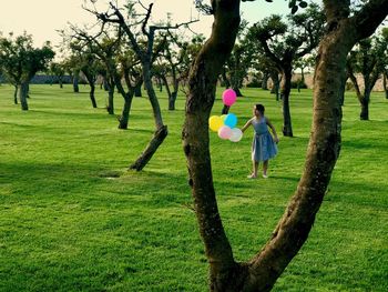 Girl playing with balloons while standing on grassy field at park