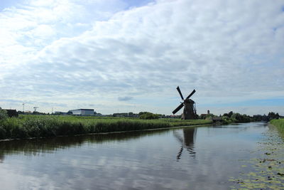 Traditional windmill by lake against sky