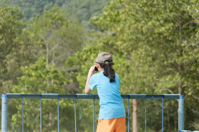 Rear view of woman standing by railing at forest