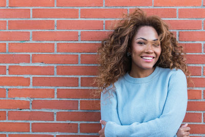 Portrait of happy young latin woman standing against brick wall with perfect smile
