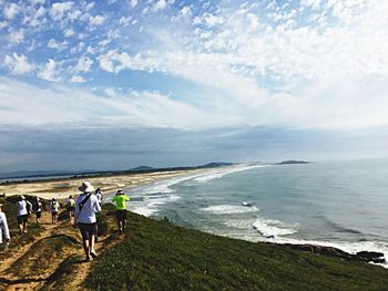 Rear view of people walking on beach against sky
