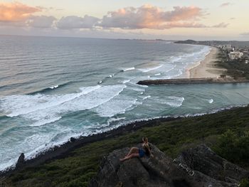 People sitting on rock by sea against sky