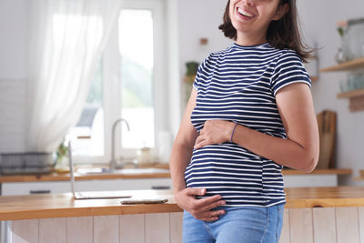 Midsection of pregnant woman standing at home