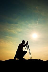 Silhouette man photographing against sky during sunset