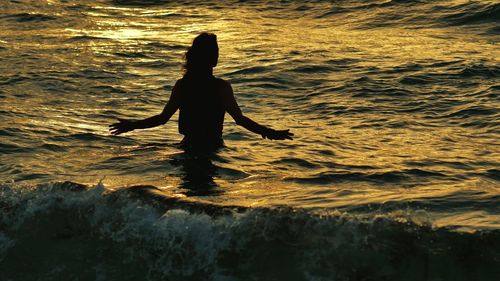 Rear view of silhouette woman in sea during sunset