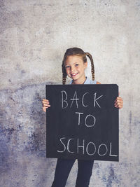 Portrait of smiling girl holding writing slate with text against wall