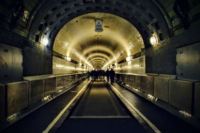People walking in illuminated tunnel at night