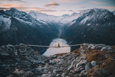 Rear view of man sitting on bridge over river against mountain