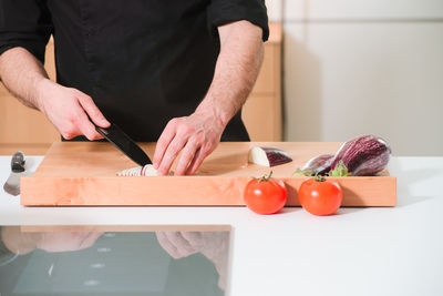 Midsection of man cutting eggplant on kitchen island