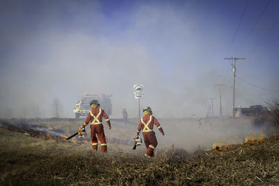 Rear view of firefighters standing on field against sky