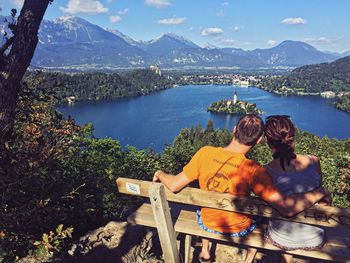 Rear view of couple sitting against lake and mountains