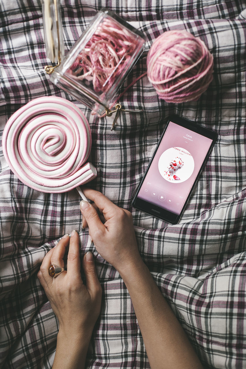 real people, human hand, holding, one person, sweet, women, human body part, hand, sweet food, indoors, lifestyles, checked pattern, food and drink, adult, pattern, lollipop, food, pink color, unhealthy eating, finger, temptation, nail