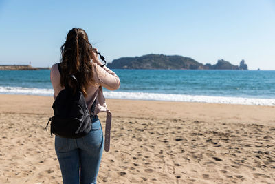 Rear view of woman standing at beach against sky