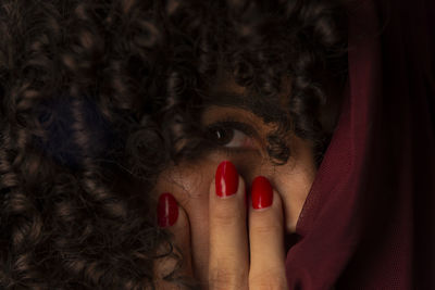 Close-up portrait of woman with red transparent cloth on her face against black background. 