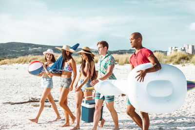 Happy friends walking on shore of beach against sky