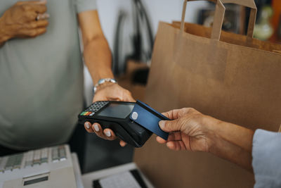 Cropped image of female customer paying through credit card to saleswoman at checkout of antique shop