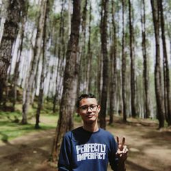 Portrait of young man gesturing while standing against trees in forest