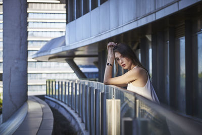 Side view of young woman standing against railing