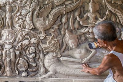 Rear view of man cleaning carving with brush