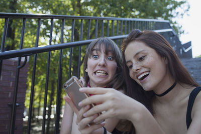 Two young women sitting on a staircase with a smart phone