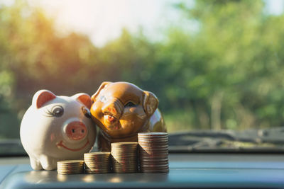 Close-up of stack of coins by piggy banks on car dashboard