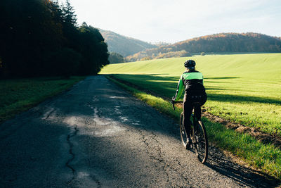 Rear view of woman riding bicycle on road against sky