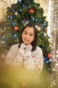 Portrait of young woman standing by christmas tree