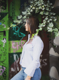 Profile view of young woman smoking while standing against graffiti wall