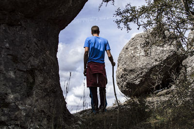 Rear view of mid adult man standing amidst rocks on field