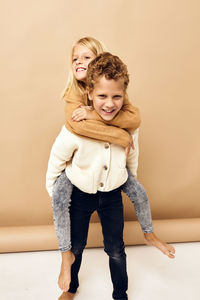 Cute sibling embracing against beige background