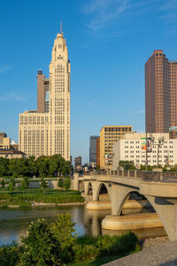 Bridge over river by buildings against sky in city