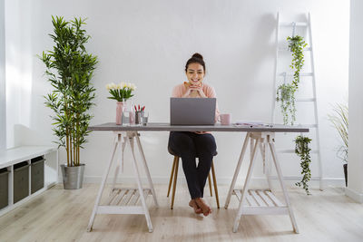 Smiling woman with hand on chin working on laptop while sitting at home