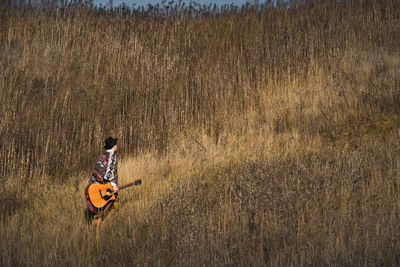 Country musician with acoustic guitar walks in grasses at a field