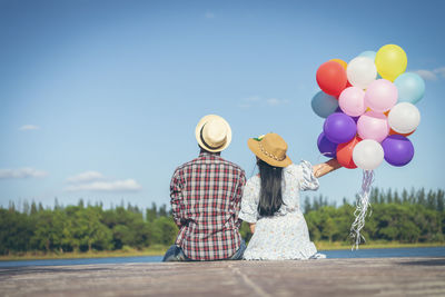 Rear view of couple with balloons against sky