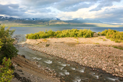 Scenic view of river by mountains against sky