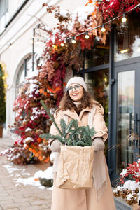 A stylish girl in a hat and coat is happy to buy a christmas nobilis in the city
