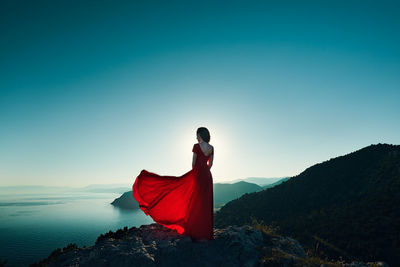 Woman with red umbrella standing on mountain against clear blue sky