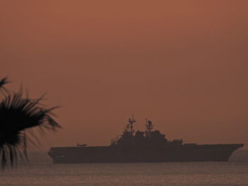 Silhouette trees by sea against orange sky