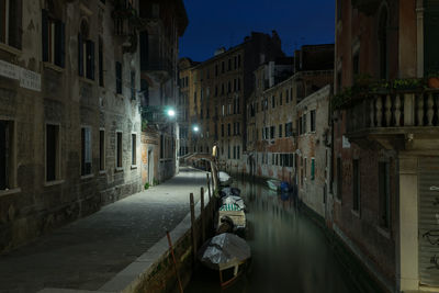 Boats moored in canal amidst buildings at night