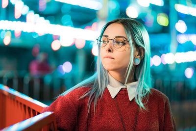 Portrait of young woman standing against illuminated wall